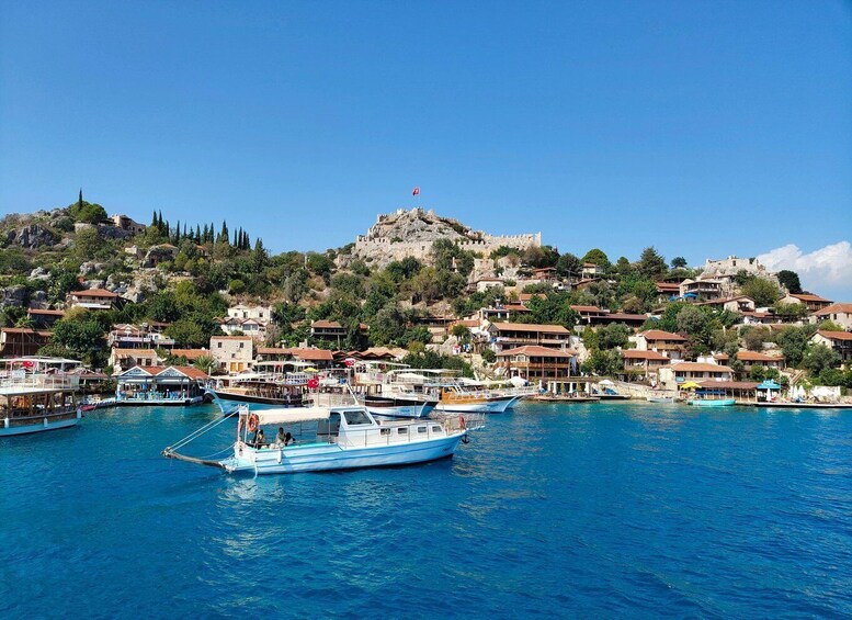 A coastal town with boats docked in the harbor, a hilltop castle, and surrounding residential buildings. 1