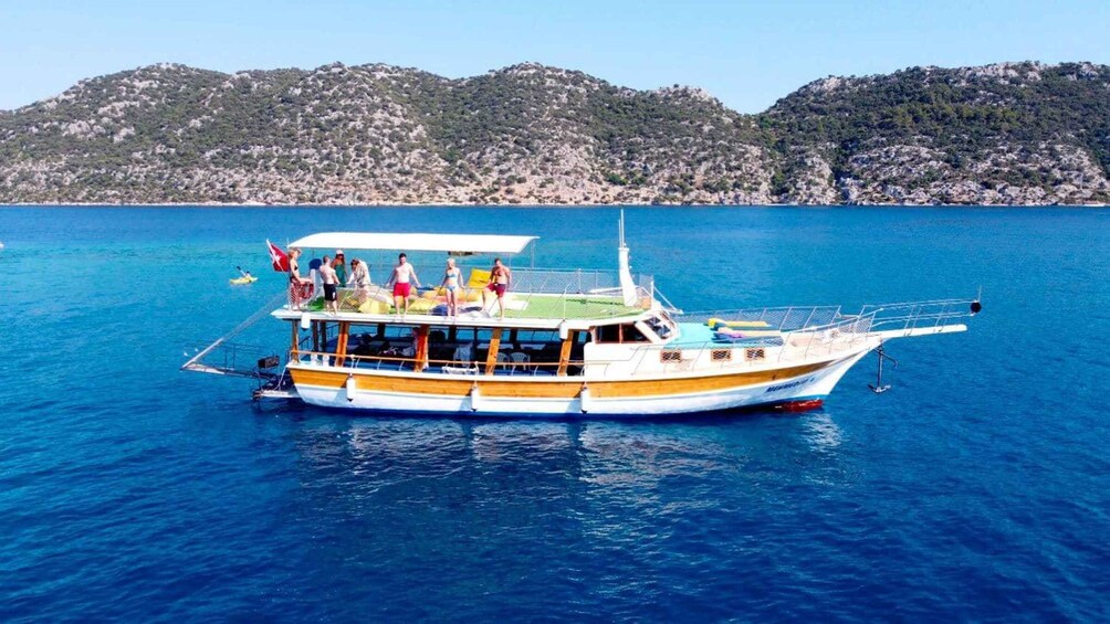 A boat with people on deck, surrounded by calm blue water and a hilly landscape in the background. 3