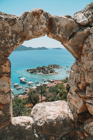 A coastal view through a stone archway, with boats docked near the shore and a rocky island in the distance. 4
