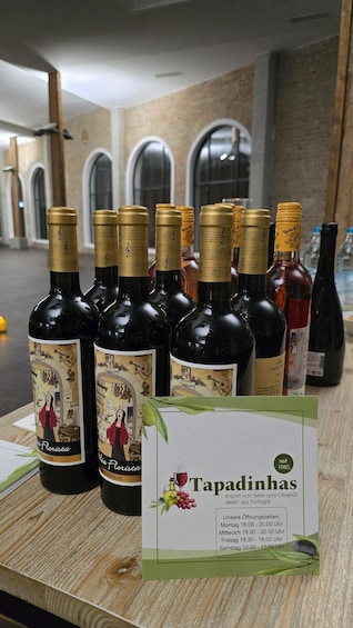 A selection of wine bottles with labels featuring musical notes and a vintage illustration, displayed on a wooden counter with a sign indicating the brand 'Tapadinhas' and pricing information. 2