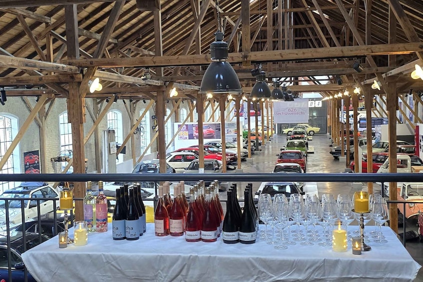 A wine tasting event with bottles and glasses on a table, under a wooden structure with hanging lights. 1