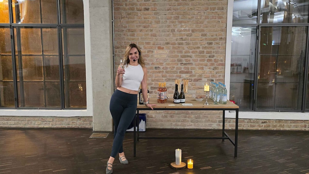 A person standing by a table with bottles and glasses, in a room with brick walls and large windows. 3