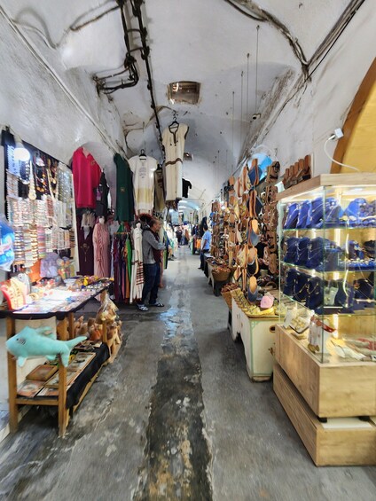 A narrow indoor market with various stalls selling jewelry, clothing, and shoes. 4