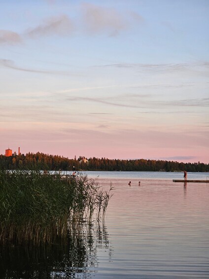 A calm lake at dusk with a dock, reeds, and a distant red building. 5