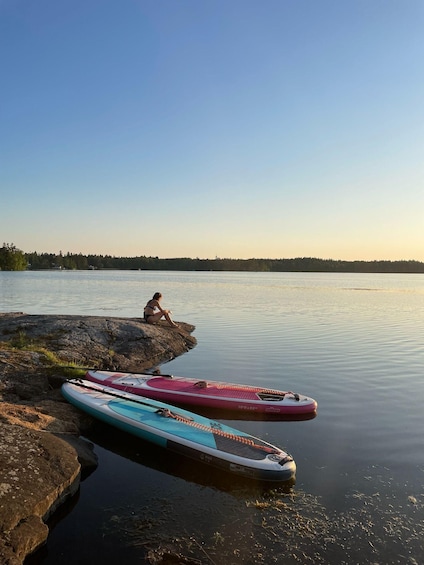 A calm lake with kayaks and a person sitting on rocks. 1