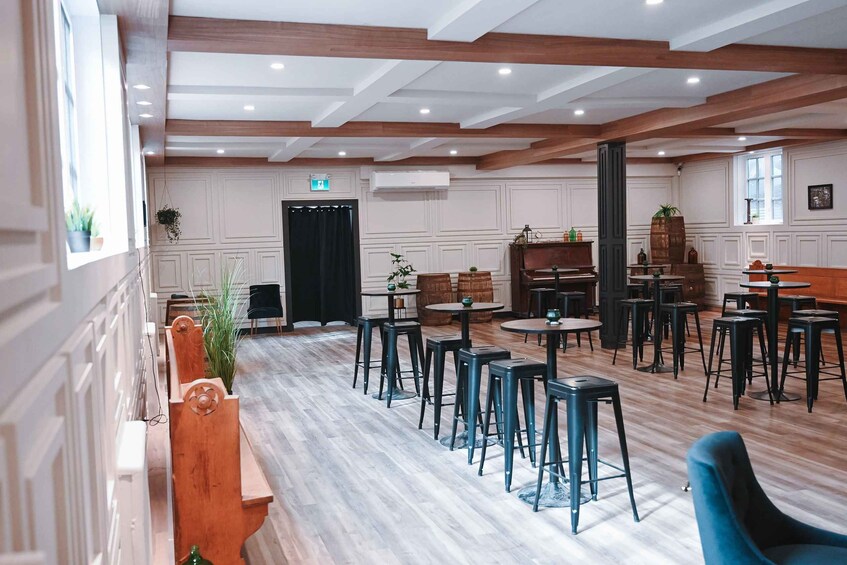 A spacious indoor area with wooden beams, white paneled walls, and multiple seating arrangements including tables and stools. 4