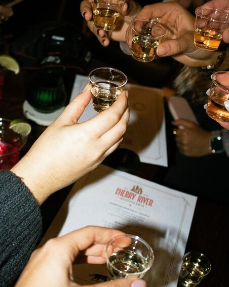 People holding shot glasses of a golden liquid, likely whiskey, at a social gathering. 3