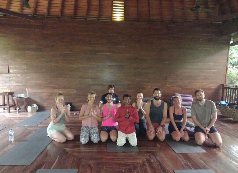 A group of people in a wooden room with yoga mats on the floor. 1