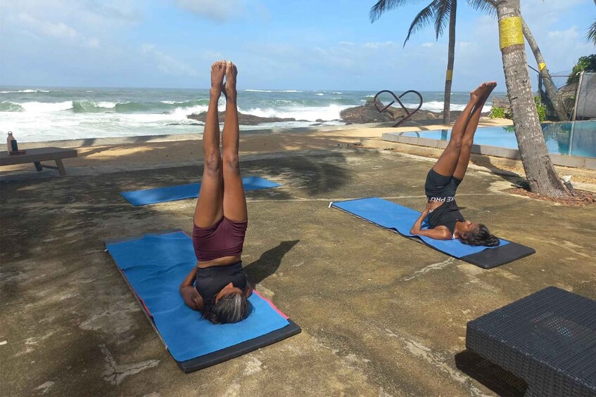 Two individuals performing handstand push-ups on blue mats at a beachside location with ocean waves in the background. 2