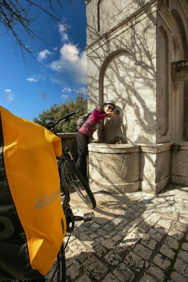 A person leaning on a stone structure with a bicycle and a yellow bag in the foreground. 1