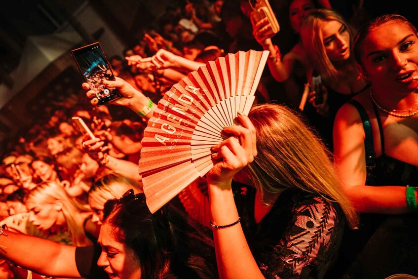 A crowd at a concert with people holding up phones and a fan. 2