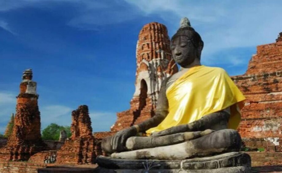 A large Buddha statue in a yellow robe, surrounded by ancient brick ruins. 3