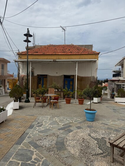 A courtyard with a tiled-roof building, potted plants, a table, and chairs. 5