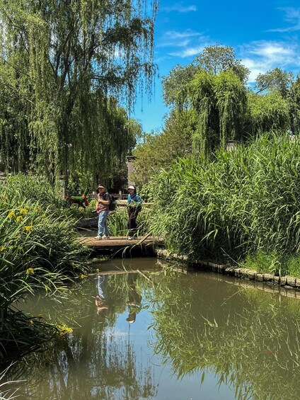 A calm river with willow trees and a wooden bridge. 1