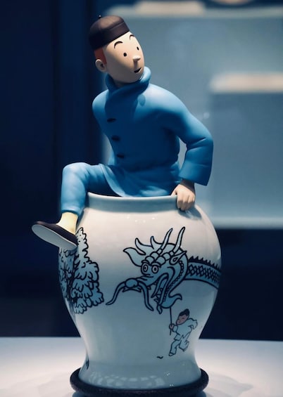 A ceramic figurine of a man in blue sitting on a vase with a dragon and a child. 2