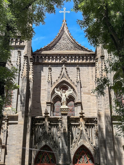 A Gothic-style church with a pointed arch window, a cross atop the roof, and intricate stone carvings. 1