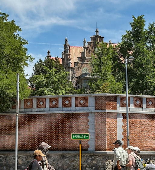 A brick wall with a green sign, a person in a cap, and a building with multiple chimneys in the background. 4