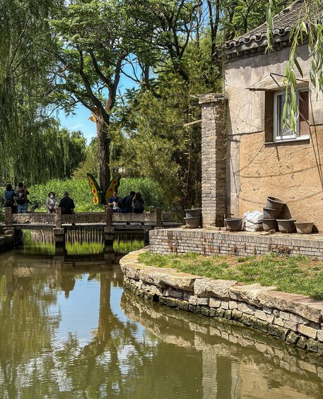 A stone bridge over a calm water body, surrounded by lush greenery and a traditional building with a tiled roof. 5