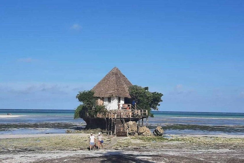 A thatched-roof house on stilts over water, surrounded by clear blue sky and calm sea. 3