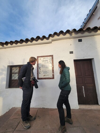 Two people standing in front of a building with a tiled roof and a door. 1