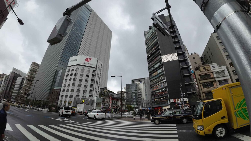 A busy urban street with tall buildings, including a prominent idemitsu building, and a yellow truck. 2
