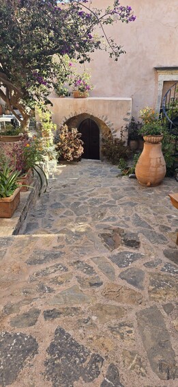 A stone-paved courtyard with a large tree, potted plants, and a rustic building with an arched entrance. 4