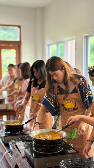 A cooking class with participants wearing aprons labeled 'A RON THAI cooking school.' 3