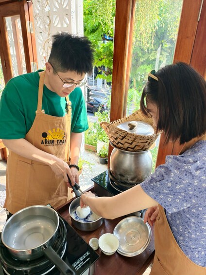 Two people cooking outdoors, one wearing an apron with a logo, and a pot on a portable stove. 2
