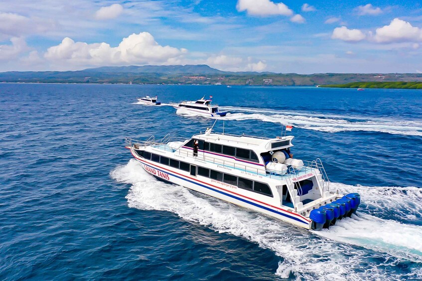 A white boat with blue and red stripes named 'Grand Tani' moving through a body of water with other boats in the background. 3