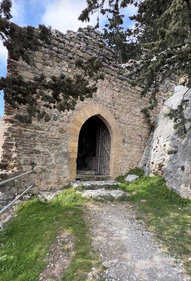 A stone archway leading into a dark interior, surrounded by grass and trees. 5