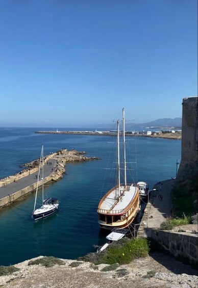A coastal scene with a historic fort, a wooden boat docked at a pier, and a sailboat in the water. 1