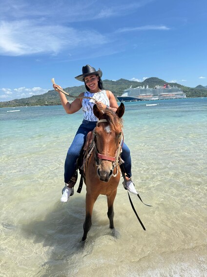 A person riding a horse in shallow water with a cruise ship in the background. 5