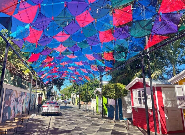 A street with colorful umbrellas overhead, a car, and colorful buildings. 2
