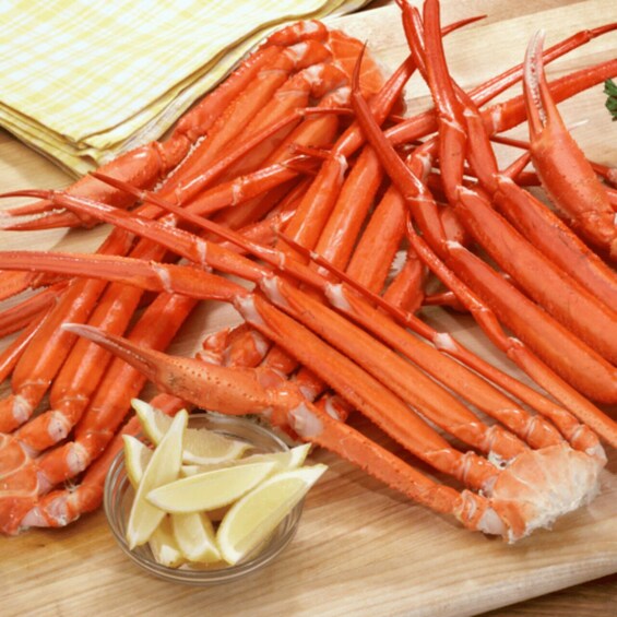 A wooden cutting board with cooked crab legs and lemon wedges. 5