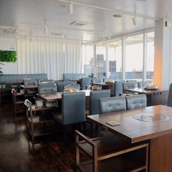A modern restaurant with wooden tables and blue chairs, large windows, and a city view. 2