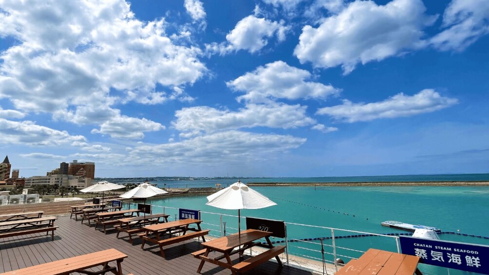 A deck with wooden benches and white umbrellas overlooking a turquoise sea. 1