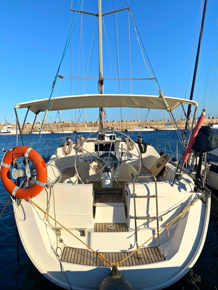 A sailboat docked at a marina with a lifebuoy, steering wheel, and deck seating. 2