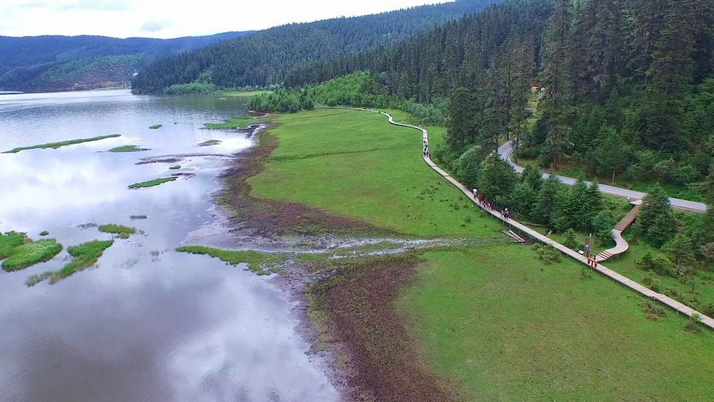 A river with a grassy bank, a forested hillside, and a winding path. 3