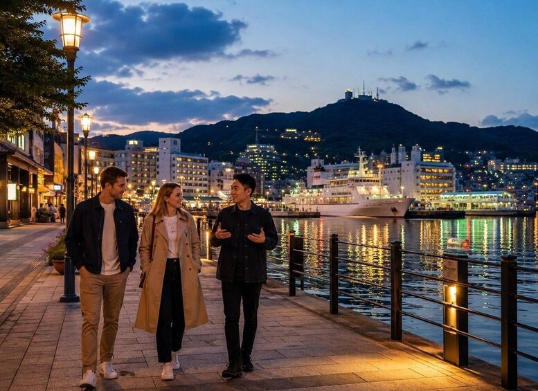 Three people walking along a waterfront promenade at dusk with city lights and a mountain in the background. 5
