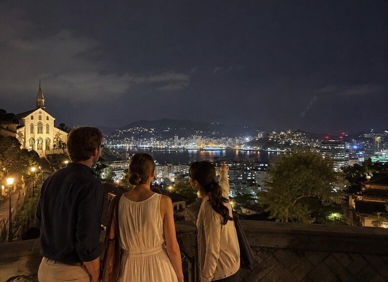 A night view of a cityscape with a river, a church, and a bridge. 1
