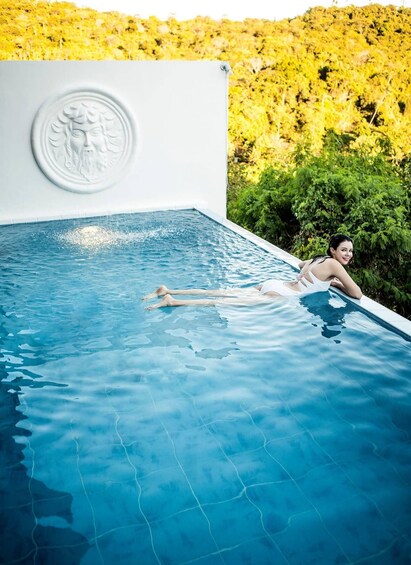 A person relaxing in a clear blue pool with a decorative wall and lush greenery in the background. 5