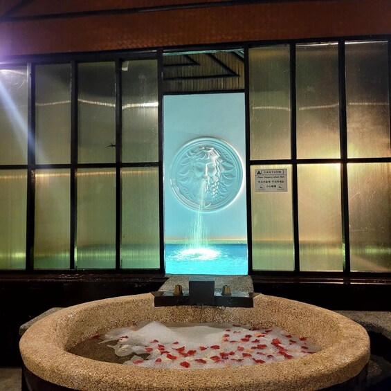 A stone basin with water and flower petals, a fountain, and a caution sign on a window. 1