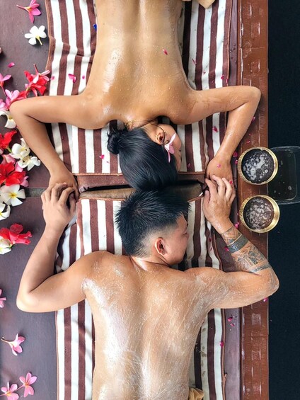 Two people receiving a massage on a striped towel with flowers around them. 3