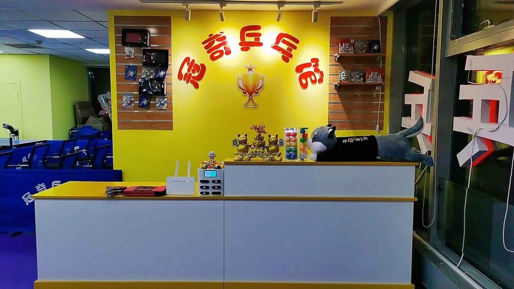 A reception desk with a yellow wall, a trophy, and various items including a plush toy. 2