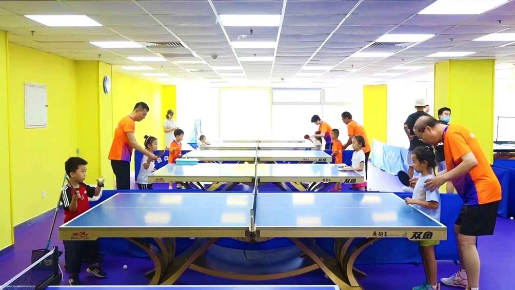 A table tennis training session with multiple tables and participants in a brightly lit room. 4