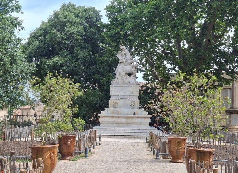 A statue-lined pathway with potted plants and a fence. 4