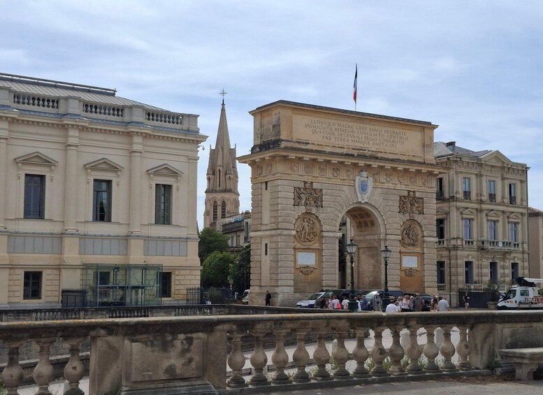 A historic building with classical architecture, a prominent archway, and a church steeple in the background. 3