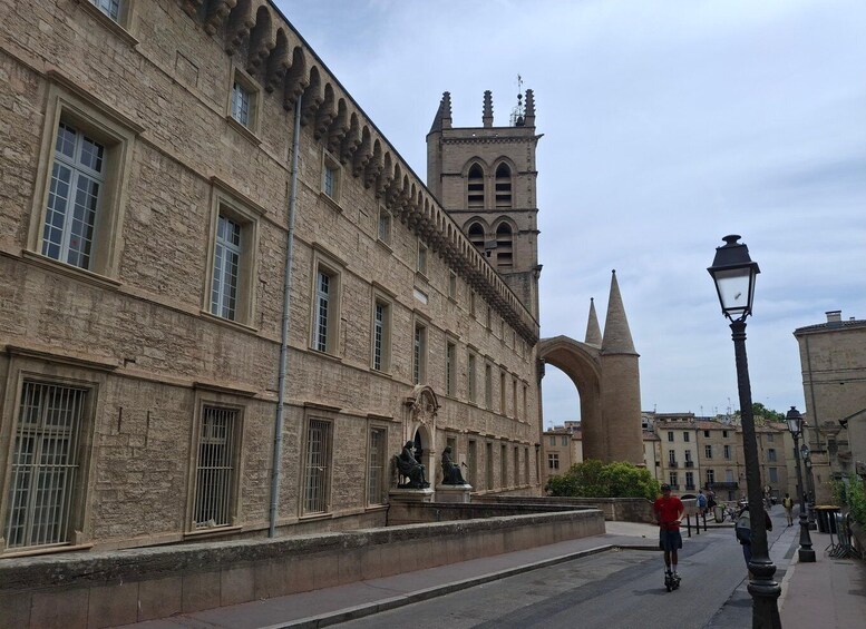 A historic stone building with a tower, a statue, and a street with pedestrians. 5