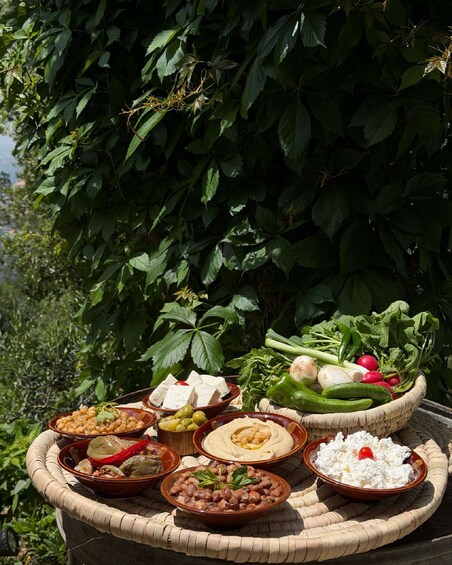A variety of Middle Eastern dishes displayed outdoors with a backdrop of dense foliage. 1