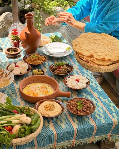 A table with various dishes, including flatbreads, hummus, and a clay pot with eggs. 3
